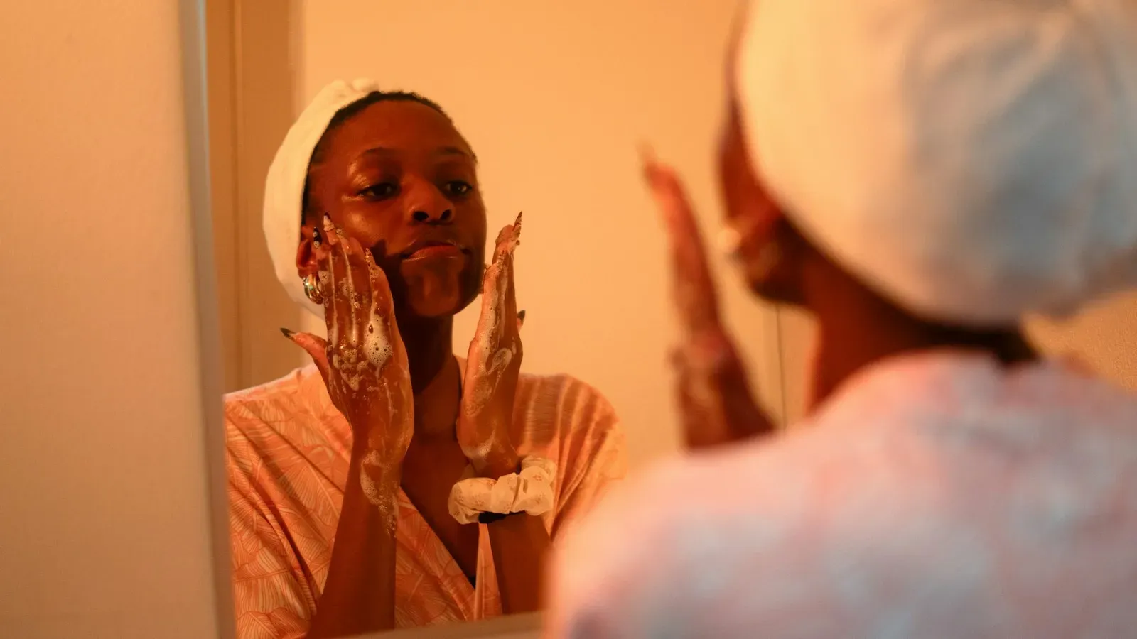 Woman washing her face with a gentle foaming cleanser in front of a bathroom mirror