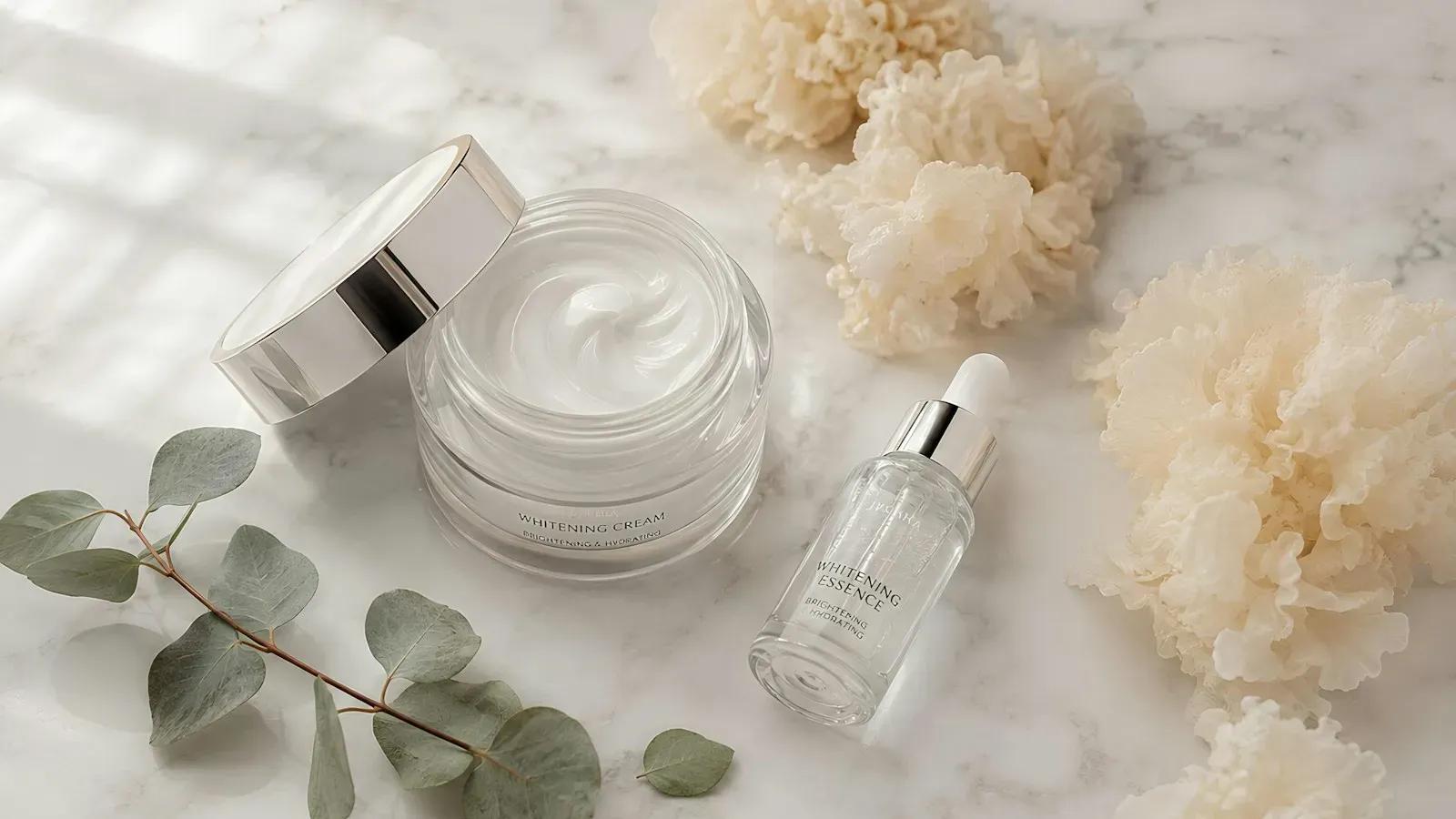 Jar of rich moisturiser with a serum bottle and eucalyptus on white marble
